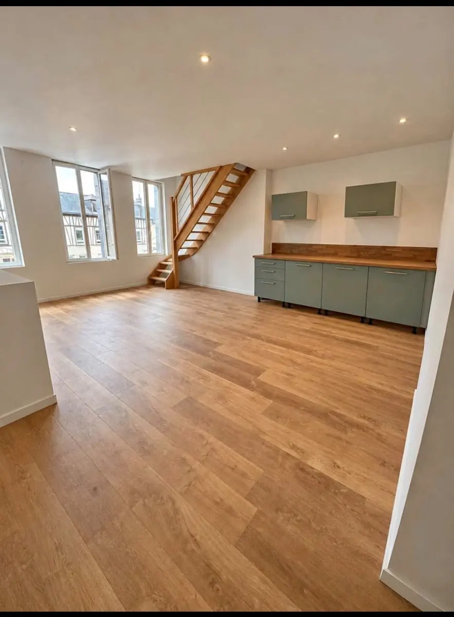 Séjour avec parquet clair, escalier et cuisine ouverte